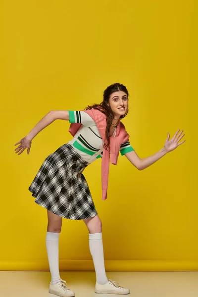 Happy woman acting like a doll, gesturing unnaturally, standing on yellow backdrop, young student — Stock Photo