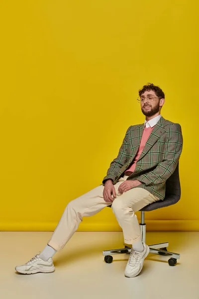 Hombre barbudo feliz sentado en la silla de la oficina, fondo amarillo, estudiante en traje de la universidad, gafas - foto de stock