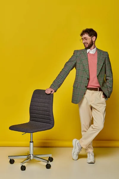 Homme positif debout avec la main dans la poche près de la chaise de bureau, fond jaune, étudiant en lunettes — Photo de stock