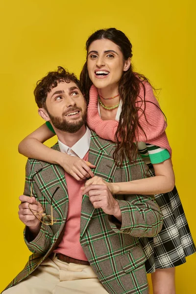 Excited woman hugging bearded man, holding glasses, yellow backdrop, college outfits, students — Stock Photo