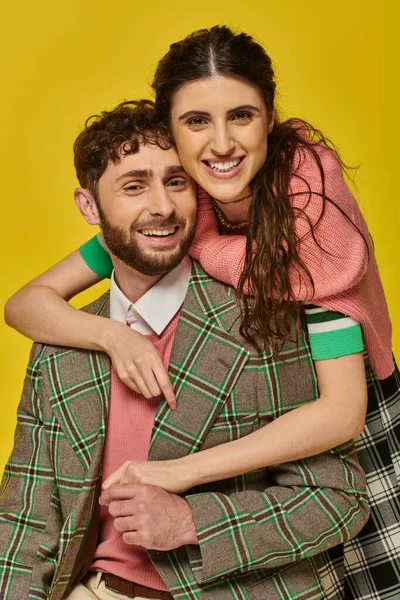 Cheerful woman hugging bearded man, in blazer, yellow backdrop, college outfits, happy students — Stock Photo