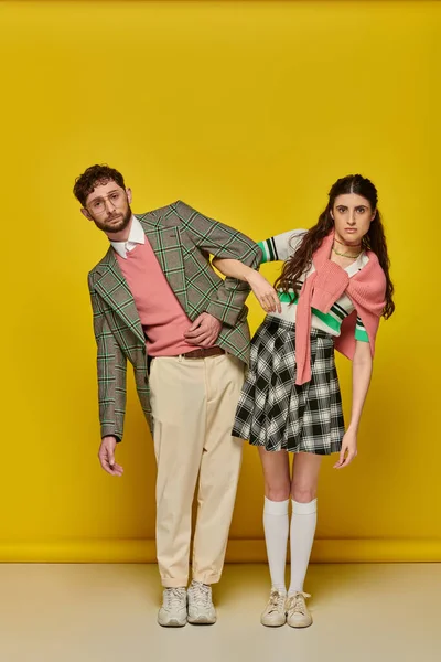 Estudiantes divertidos, pareja de pie sobre fondo amarillo, hombre y mujer en trajes universitarios, ropa académica - foto de stock