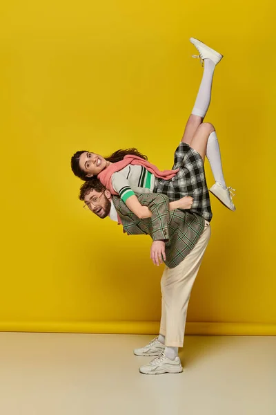 Funny couple, joyful man in glasses lifting woman, piggybacking, students in college wear, together — Stock Photo