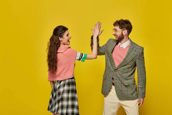 Estudiantes emocionados dando cinco altos en el fondo amarillo, hombre y mujer felices en ropa de la universidad, elegante - foto de stock