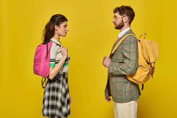 Students standing with backpacks, face to face, looking at each other, yellow backdrop, college — Stock Photo