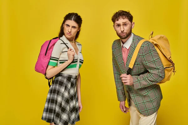 Curious students standing with backpacks, looking at camera, yellow backdrop, college outfits, study — Stock Photo