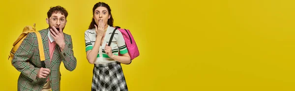 Shocked students standing with backpacks, looking at camera, covering mouth, yellow backdrop, banner — Stock Photo