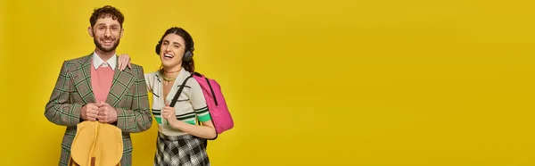 Cheerful woman in wireless headphones standing near bearded man, students holding backpacks, banner — Stock Photo