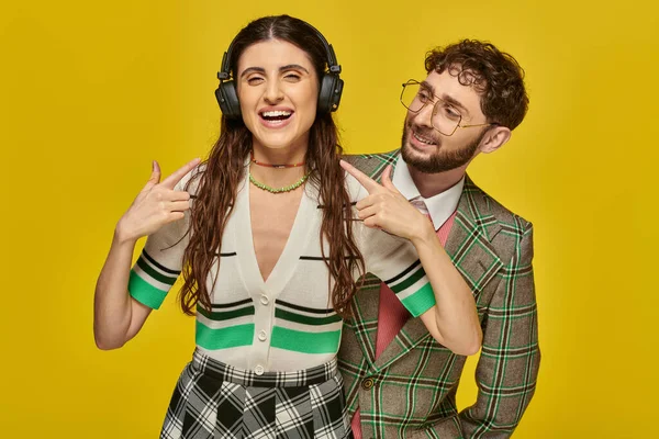Cheerful woman pointing at wireless headphones, listening music near bearded man, college students — Stock Photo