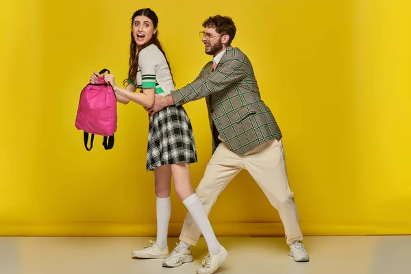 Estudantes engraçados, homem brincalhão abraçando cintura de colega de classe feminina no fundo amarelo, vida universitária — Fotografia de Stock