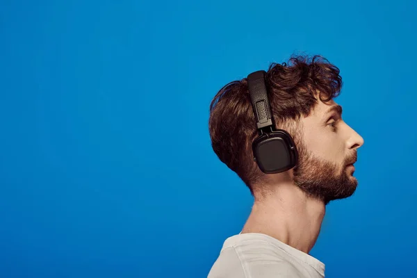 Seitenansicht, Mann mit drahtlosem Kopfhörer, der Musik auf blauem Hintergrund hört, Männermode, Playlist — Stockfoto