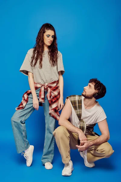 Stilvolles Paar, Studenten in Freizeitkleidung, Kopfhörer, Musik, fettes Make-up, blauer Hintergrund — Stockfoto