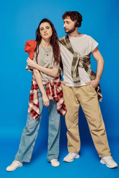 Stilvolles Paar, Kopfhörer, Musik, Streetwear, fettes Make-up, Frau mit Baseballkappe, blauer Hintergrund — Stockfoto