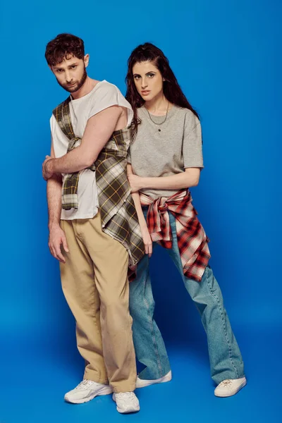 Casal posando em desgaste de rua, fundo azul, mulher com maquiagem ousada de pé com homem barbudo, estilo — Fotografia de Stock