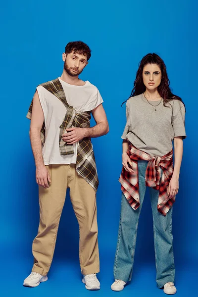 Paar posiert in Freizeitkleidung, blauer Hintergrund, Frau mit fettem Make-up steht mit bärtigem Mann, Trend — Stockfoto