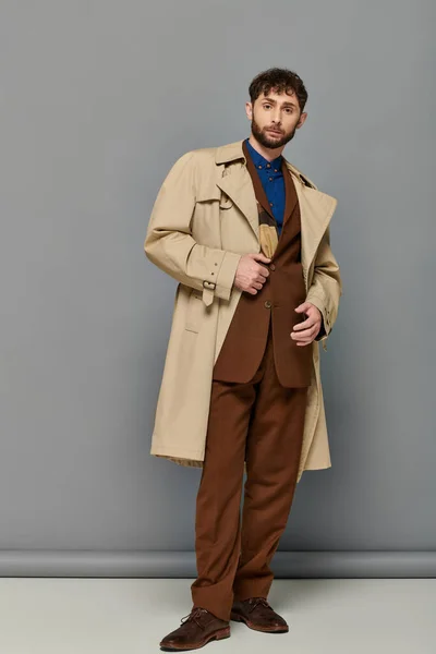 Vêtements de dessus, homme barbu en trench coat posant sur fond gris, couches confortables, mode automne — Photo de stock