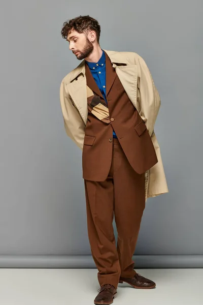 Верхній одяг, стильний чоловік в траншеї пальто позує на сірому тлі, затишні шари, осінь мода — Stock Photo