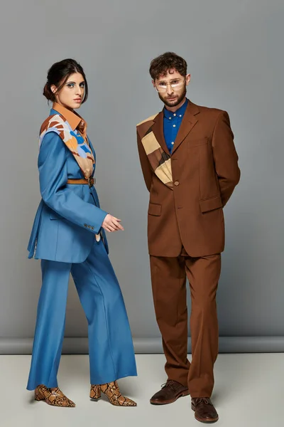 Couple branché, tournage de mode, homme et femme en costumes posant sur fond gris, brun, bleu, style — Photo de stock