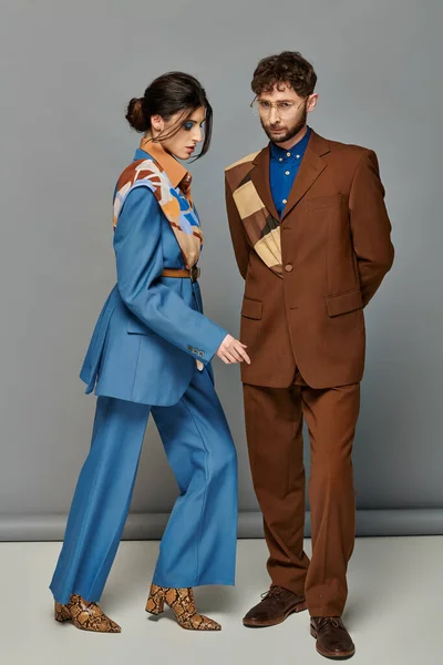 Модная пара, мужчина и женщина в костюмах позируют на сером фоне, коричневый, синий, модные съемки — стоковое фото