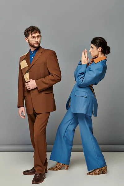 Модная поза, модели в формальной одежде на сером фоне, мужчина и женщина в костюмах, модная съемка — стоковое фото
