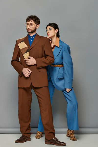 Модели в костюмах, позирующие на сером фоне, шикарные мужчина и женщина в сшитых по заказу формальных нарядах — стоковое фото