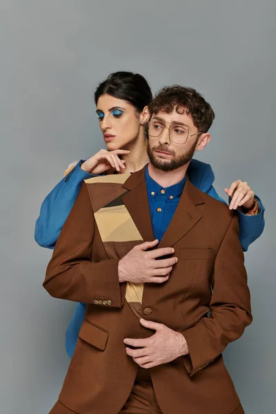 Homme et femme élégants en costumes posant sur fond gris, style élégant, tenue formelle, maquillage audacieux — Photo de stock