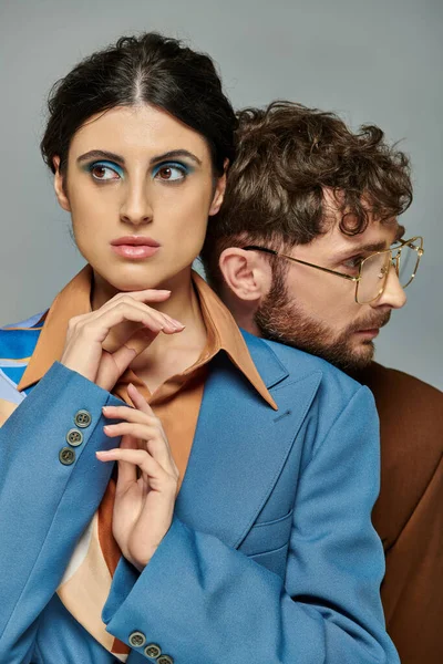 Trendpaar posiert auf grauem Hintergrund, Anzüge, eleganter Stil, Frau mit kühnem Make-up, bärtiger Mann — Stockfoto