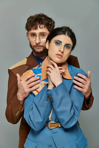 Bärtiger Mann mit Brille umarmt Frau, Models in trendigen Anzügen, grauer Hintergrund, Porträt — Stockfoto