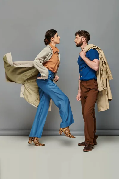 Bewegung, brünette Frau in Animal-Print-Stiefeln, die neben stylischem Mann läuft, graue Kulisse, Oberbekleidung — Stockfoto