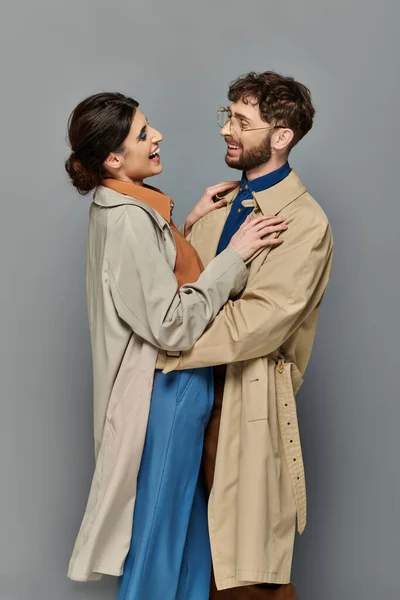Temporada de outono, homem feliz e mulher abraçando no fundo cinza, casal em casacos de trincheira, estilo, romance — Fotografia de Stock