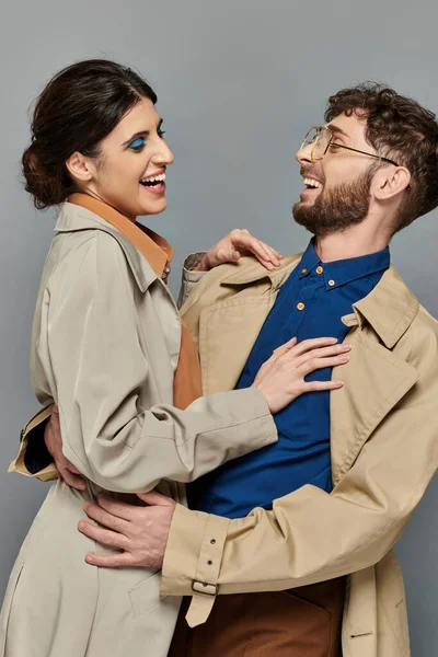 Stagione autunnale, uomo e donna gioiosi che si abbracciano su sfondo grigio, coppia in trench, stile, romanticismo — Foto stock