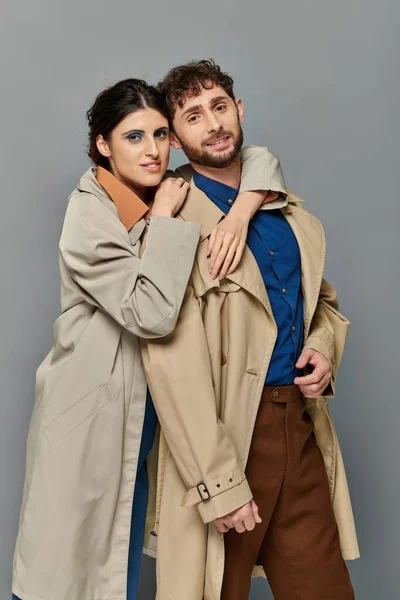 Temporada de otoño, sonrisa, hombre y mujer abrazándose sobre fondo gris, pareja en abrigos de trinchera, estilo, romance - foto de stock