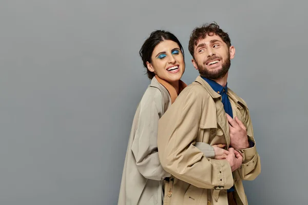 Fall season, smile, romantic couple hugging on grey background, trench coats, style, bold makeup — Stock Photo