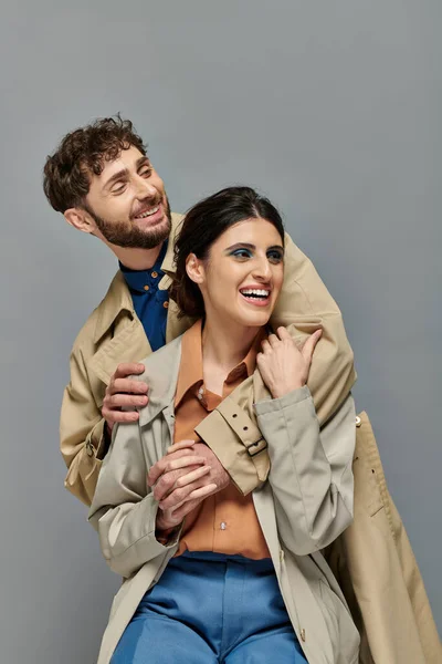 Fröhliches Paar, Oberbekleidung, Herbstzeit, grauer Hintergrund, Mann und Frau in Trenchcoats, Stil — Stockfoto