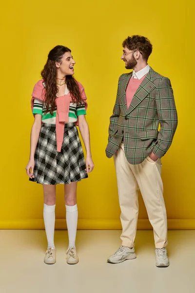 Estudiantes positivos mirándose el uno al otro en el fondo amarillo, hombre y mujer felices en trajes universitarios - foto de stock