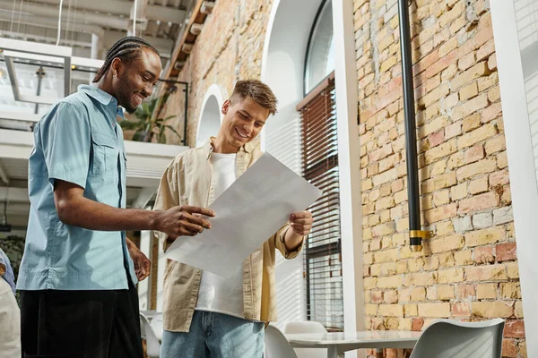 Happy african american man looking at project with colleague, office workers, startup, generation z — Stock Photo