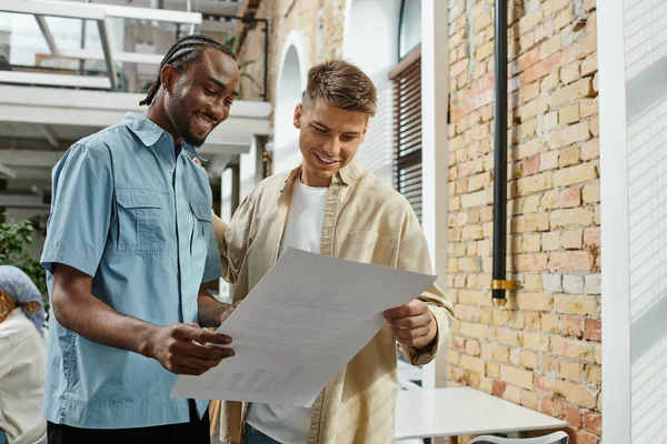 Happy interracial man looking at project with colleague, office workers, startup, generation z — Stock Photo