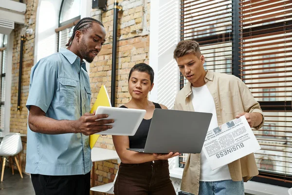 Compañeros de trabajo interracial celebración de gadgets, ordenador portátil, tableta, era digital, puesta en marcha, hombres y mujeres, oficina - foto de stock