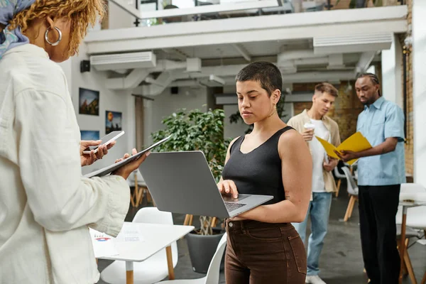 Jóvenes compañeros de trabajo multiculturales, mujer con tatuaje utilizando el ordenador portátil, generación z, puesta en marcha, coworking - foto de stock