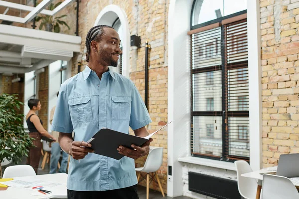 Happy african man holding folder, analyzing project, looking at window, coworking, startup — Stock Photo