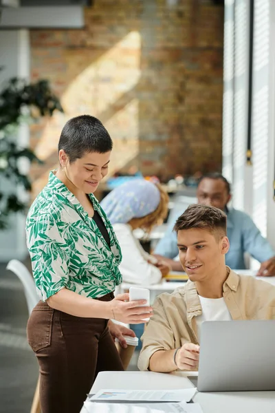 Cheerful woman showing smartphone to colleague, laptop, coworking, gen z, tattoo: love, graphs, blur — Stock Photo