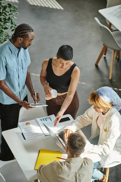 Four multicultural business people working on startup ideas in coworking, gadgets and graphs — Stock Photo
