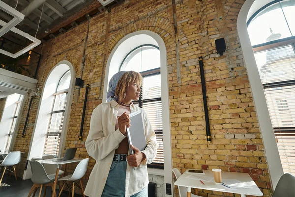 Pensive african american woman with braces smiling, holding folders in open space coworking, startup — Stock Photo