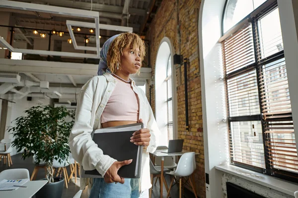 African american woman holding folders in open space, startup project, thinking, looking at window — Stock Photo