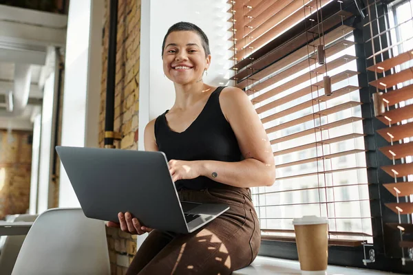 Happy tattooed woman using laptop, sitting on windowsill, coffee to go, startup project, coworking — Stock Photo