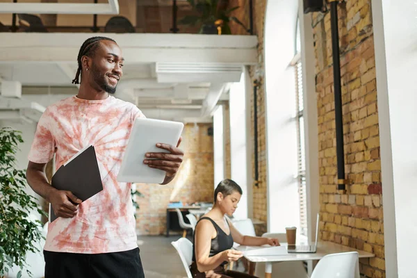 Happy african american man holding tablet, folder, working near female coworker, startup project — Stock Photo