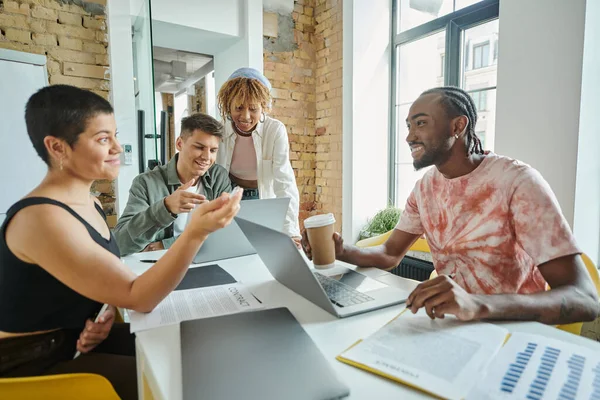 Des gens d'affaires divers discutant des idées de démarrage et souriant près de gadgets, coworking, leadership — Photo de stock