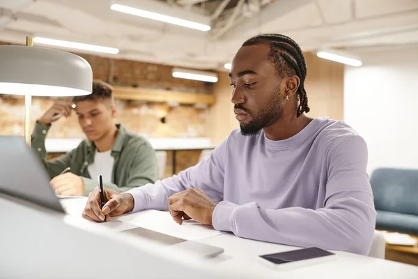 Open space, african american man taking notes, writing down ideas near laptop, startup planning — Stock Photo