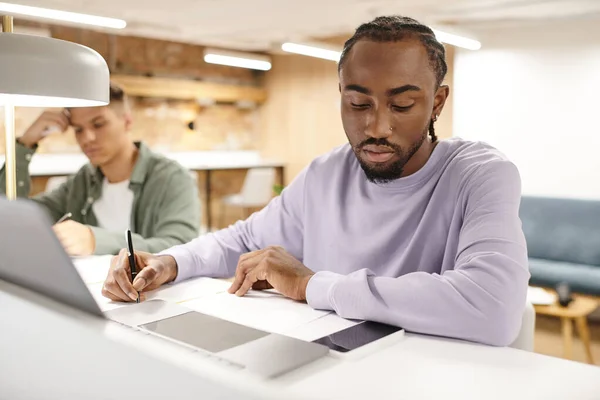 Coworking, homem americano africano tomando notas, escrevendo ideias perto de gadgets, planejamento de inicialização — Fotografia de Stock