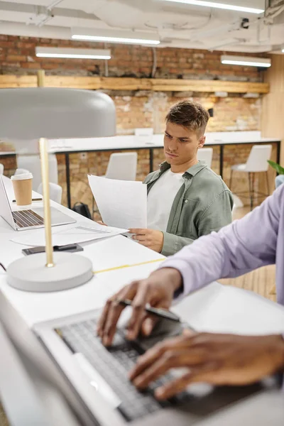 Homem concentrado verificando documentos, trabalhando no escritório, diversidade, coworking, laptops, startup — Fotografia de Stock